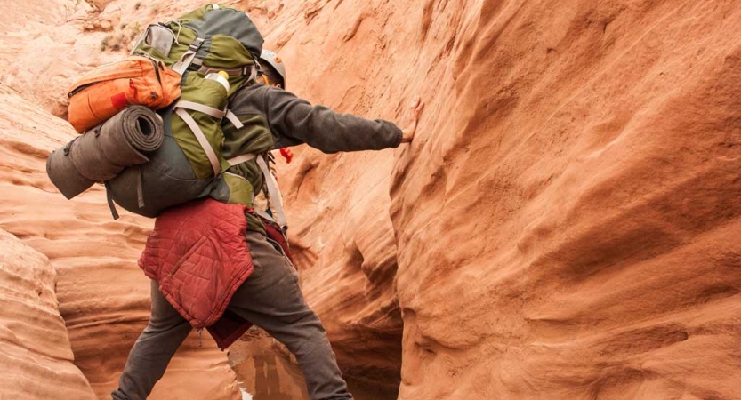 A person wearing a backpack makes their way through a red slot canyon. 